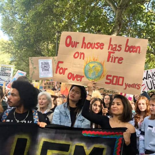 Protesters at the Global Climate Strike with a banner that states "Our House Has Been on Fire for Over 500 years"